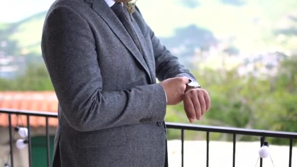 Um homem em um terno elegante fica na varanda e endireita a manga de sua jaqueta — Vídeo de Stock