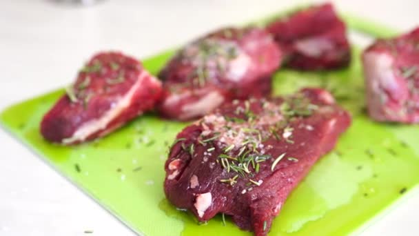 Pezzi di bistecca cruda su un tagliere verde, cosparso di sale e rosmarino, versato con olio di girasole. — Video Stock