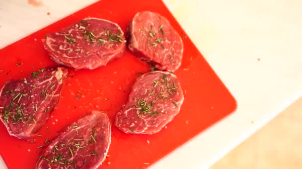 Пять кусочков сырого мяса стейка на красной доске, посыпанной розмарином и грубой солью. — стоковое видео