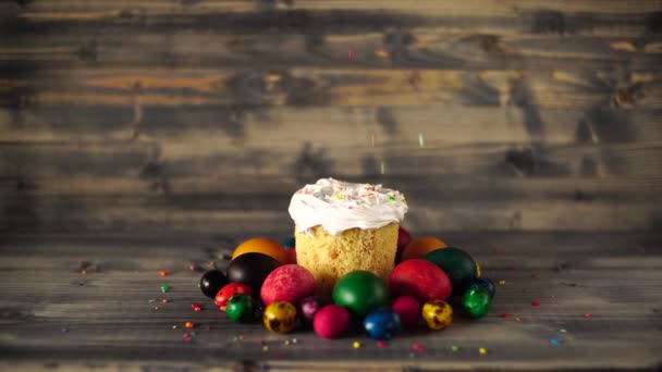 Pastel de Pascua con esmalte blanco se espolvorea con polvo multicolor. Pollo pintado multicolor y huevos de codorniz sobre un fondo de madera. — Vídeos de Stock