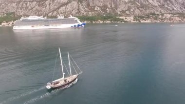 Kotor Körfezi 'nin ortasındaki büyük bir yolcu gemisine yelken açan bir yat.