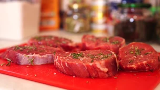 Cinco trozos de carne cruda de filete en una tabla de cortar roja, espolvoreado con romero y sal gruesa. — Vídeos de Stock