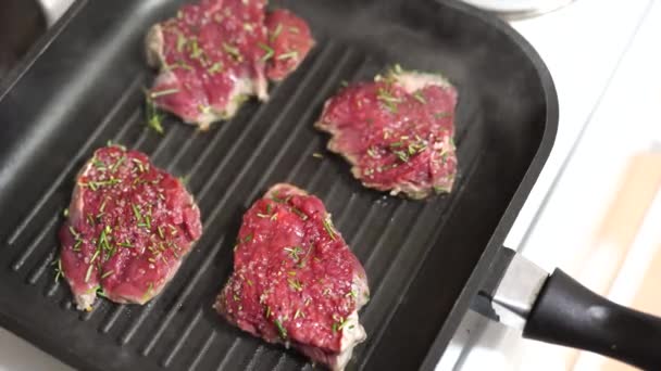 Cuatro filetes crudos se fríen en una sartén a la parrilla. — Vídeos de Stock