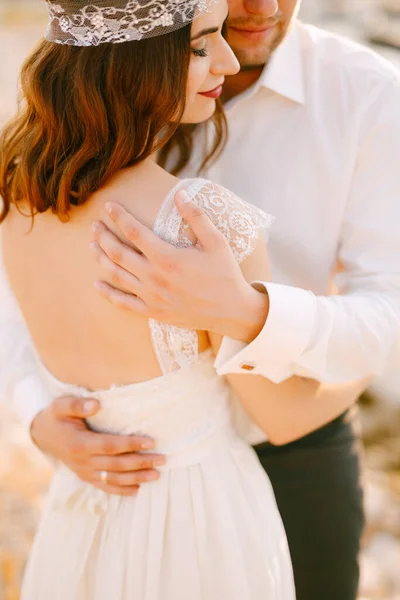 The bride and groom tenderly hug , the groom put his hands on the back of the bride