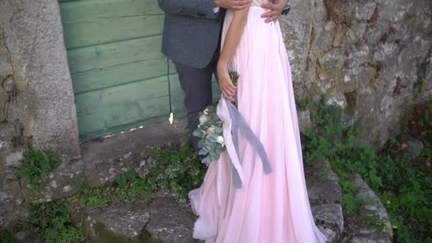 Brudgummen kramar bruden i en vacker klänning med öppen rygg och stryker hennes hand, bruden håller en bukett i handen — Stockvideo