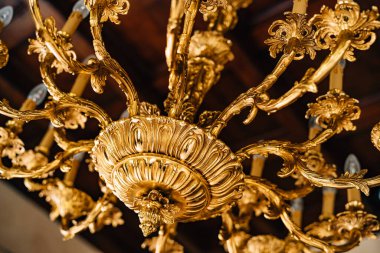 Altın bir avizeye yakın çekim. Şamdanları ve desenleri olan bir avize.