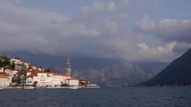 Karadağ 'ın Perast kasabası. Denizde yelken açan bir teknenin görüntüsü. Şehir, dağların arka planına ve bulutlu gökyüzüne karşı. Seyahat arkaplanı.