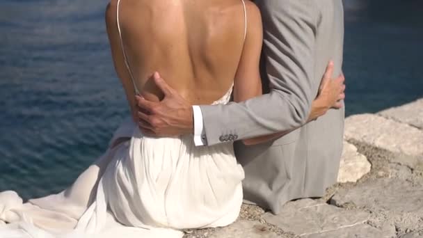 Bruden og brudgommen som sitter og klemmer på brygga og ser på Perast . – stockvideo