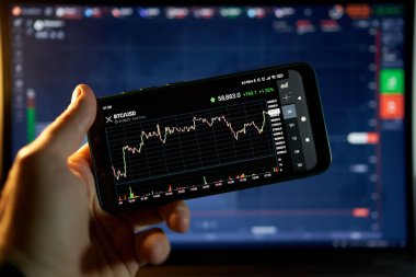 Venedik, İtalya - 06 Nisan 2021: Akıllı telefondaki borsa yatırımlarını analiz eden yatırımcı. Akıllı telefondan hisse senedi ticareti yapan biri. Bitcoin oranı Nisan 2021 'de 58 bin dolardan fazladır..