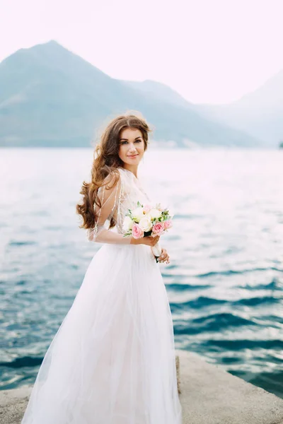 Η νύφη κρατά ένα μπουκέτο τριαντάφυλλα στα χέρια της και στέκεται στην προβλήτα στον κόλπο του Κότορ. — Φωτογραφία Αρχείου