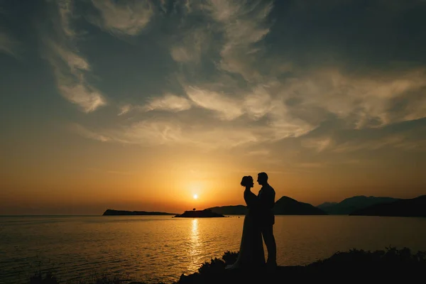 Gli sposi si abbracciano in riva al mare al tramonto e si guardano — Foto Stock