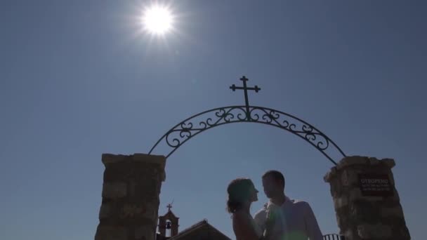 Los novios se besan y abrazan en el arco forjado cerca de la Iglesia de Sveti Savva en Montenegro — Vídeo de stock