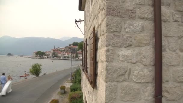 Perast, Montenegro - 10 de julho de 2020: a noiva e o noivo caminham lado a lado de mãos dadas no cais na cidade velha de Perast — Vídeo de Stock