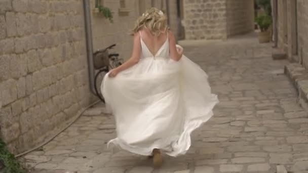 Perast, Montenegro - 11 luglio 2020: La sposa in un abito delicato corre per la strada della città vecchia, tenendo la gonna — Video Stock