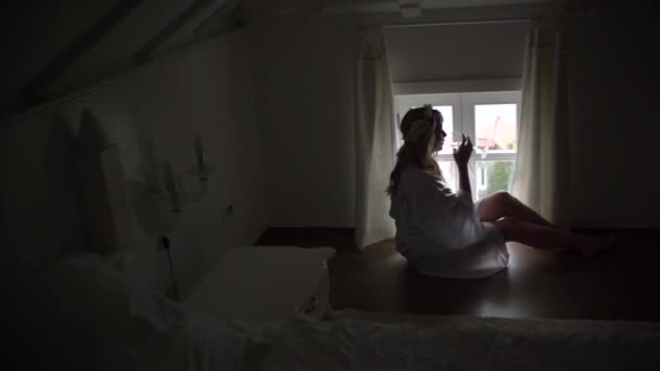 Perast, Montenegro - 11 july 2020: Silhouette of a woman sits at the window in the hotel room in a robe with a glass of champagne — Stock Video