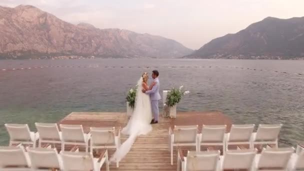 Perast, Montenegro - 11 juli 2020: Bruden och brudgummen står nära bröllopsplatsen på piren vid havet, med utsikt över bergen — Stockvideo
