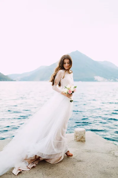 Η νύφη κρατά ένα μπουκέτο τριαντάφυλλα στα χέρια της και στέκεται στην προβλήτα στον κόλπο του Κότορ. — Φωτογραφία Αρχείου