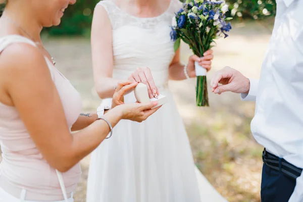 花嫁は新郎の指にそれを置くために新婦付添人が保持する箱から結婚指輪を取ります — ストック写真