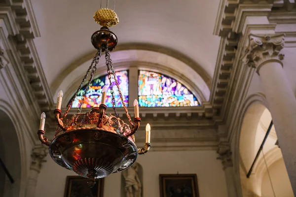 Chandelier in the Empire style under the ceiling in the church, against the background of a window with a mosaic. An antique massive chandelier hangs on chains with electric candles. — Stock Photo, Image