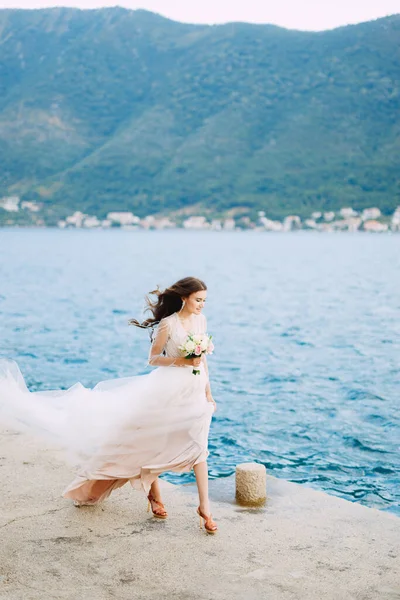 Η νύφη κρατά ένα μπουκέτο τριαντάφυλλα στα χέρια της και περπατά κατά μήκος της προβλήτας στον κόλπο του Κότορ — Φωτογραφία Αρχείου