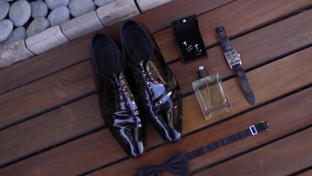 Lacquered mens shoes, wrist watch, perfume, cufflinks, bow tie on wooden background — Stock Video