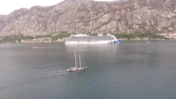 Kotor, Montenegro - 29 july 2020: A sailing yacht sails to a large cruise ship in the middle of the Bay of Kotor — Stock Video