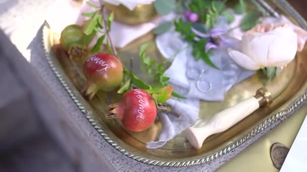 Wedding rings, young pomegranates with names written on them, wax seal, rosebuds and green twigs on a shiny silver tray — Stock Video