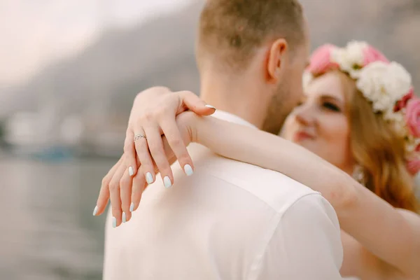 La novia y el novio se abrazan en el muelle, la novia en una delicada corona envolvió sus brazos alrededor del cuello de los novios — Foto de Stock