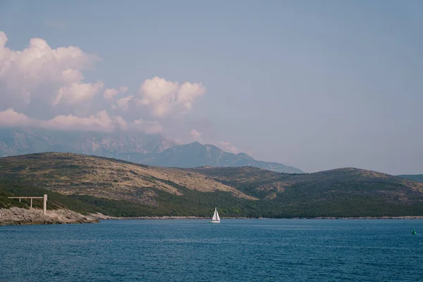 A white sailboat sails on the background of Mount Lovcen on blue water. — Stock Photo, Image