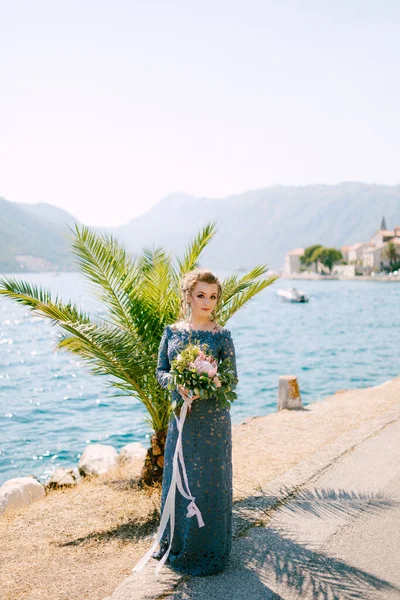 Bruden i en snygg grå klänning står med bröllopsbuketter på piren nära gamla stan i Perast — Stockfoto