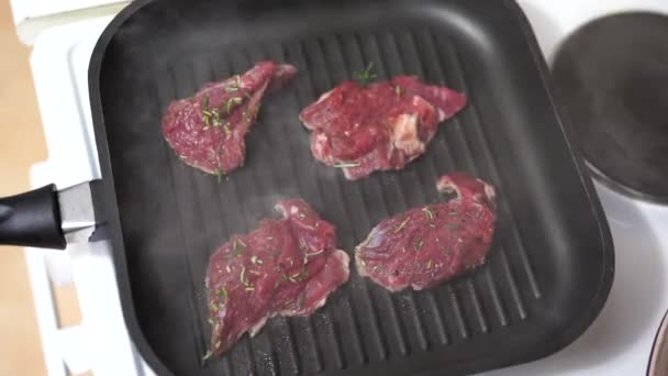 Cuatro filetes crudos se fríen en una sartén a la parrilla. — Vídeos de Stock