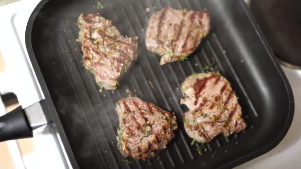 Vier geröstete Steaks auf einer gegrillten Pfanne mit fein gehacktem Rosmarin. — Stockvideo