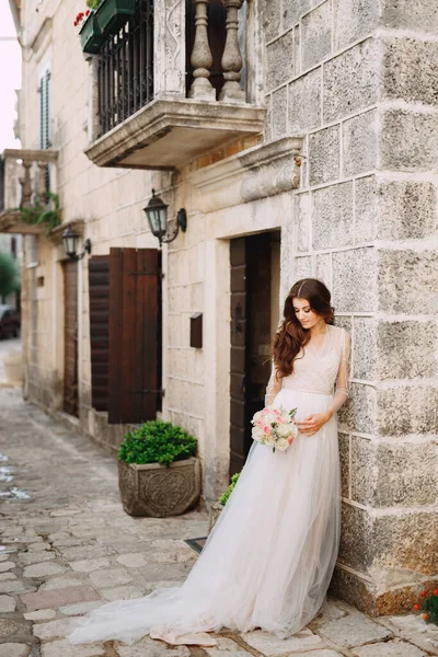 Una sposa con un bouquet di nozze si trova in un bellissimo edificio antico su un'accogliente strada Perast — Foto Stock