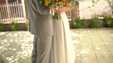 Gelin ve damat eski şehrin gölgeli caddesinde sarılıyor, gelin bir buket tutuyor. 
