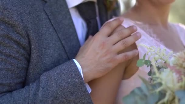 De bruidegom knuffelt de bruid streelt haar hand, de bruid houdt een boeket in haar handen — Stockvideo