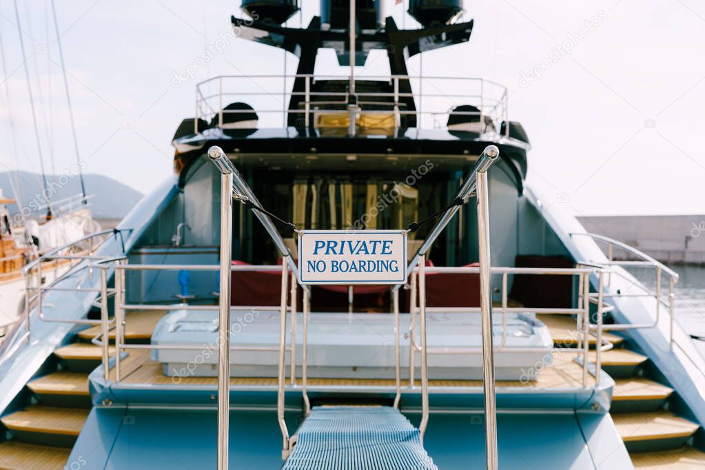 Stern trawl of a beautiful motor white yacht with a wooden ladder. Inscription: PRIVATE No Boarding. Close-up
