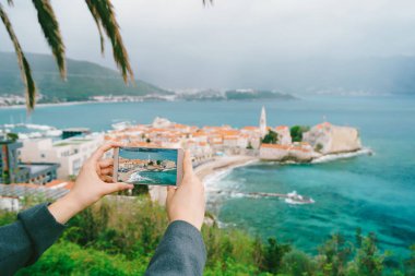 Elinde bir fotoğraf olan akıllı telefon, Karadağ 'ın eski kentinin arka planında yer alıyor.