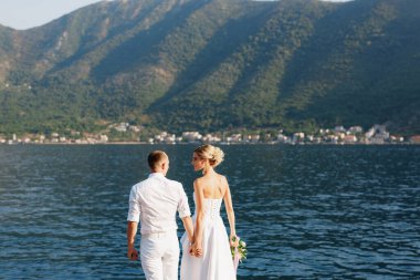 Gelin ve damat, Kotor Körfezi kıyısında el ele tutuşuyorlar. 