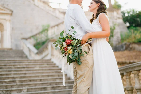 Sposa e sposo che si abbracciano sull'antico campanile vicino alla chiesa di Prcanj, sposa che tiene in mano il bouquet nuziale — Foto Stock