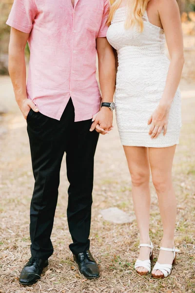 Un homme en chemise rose et une femme en robe blanche courte se tiennent côte à côte et tiennent tendrement la main — Photo