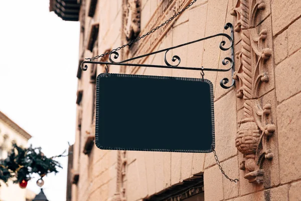 Stylish rectangular blank sign in a wrought-iron frame hangs on the stone wall of an ancient building