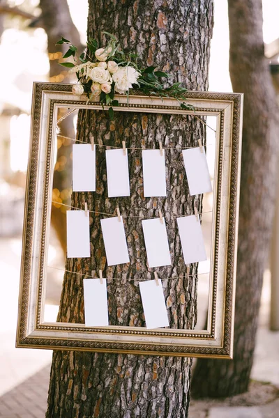 Blanks for the wedding guest list hang in a beautiful frame on a tree. Seating plan