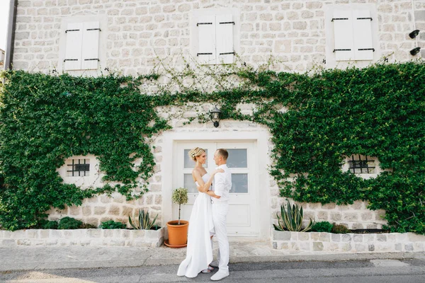 Das Brautpaar steht umarmt in einem schönen, mit Efeu bewachsenen weißen Haus in der Altstadt von Perast — Stockfoto