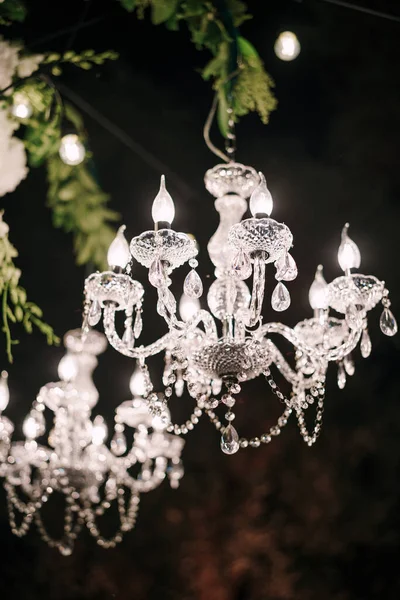 Crystal clear chandeliers with candlesticks and candelabra, candle light bulbs, glass pendants and crystals. In the dark on black. background at night. — Stock Photo, Image