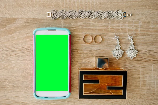 Smartphone dengan layar kosong terletak di meja kayu di samping anting-anting, cincin, gelang dan parfum — Stok Foto