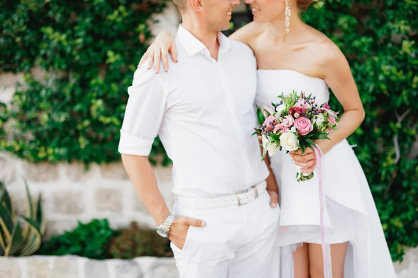 La novia y el novio se abrazan en una hermosa casa blanca cubierta de hiedra en el casco antiguo de Perast, de cerca — Foto de Stock