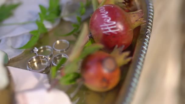 Wedding rings, young pomegranates with names written on them, rosebuds and green twigs on a shiny silver tray — Stock Video