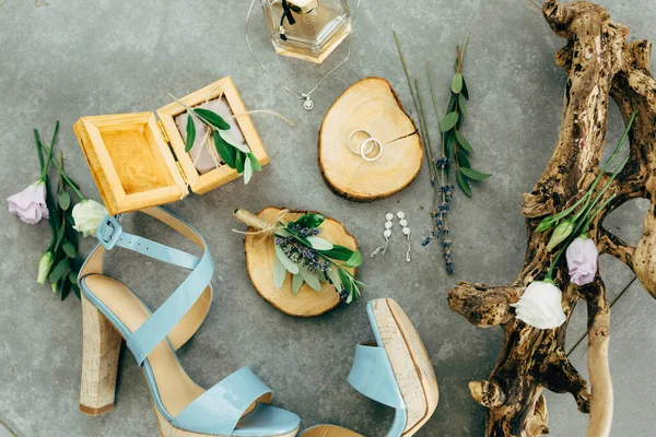 Anillos de boda se encuentran en un soporte de madera rodeado de sandalias con tacones, caja de madera, perfume, flores y ramitas en el suelo — Foto de Stock