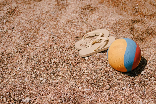 Pelota multicolor y chanclas de color beige yacen en la playa —  Fotos de Stock