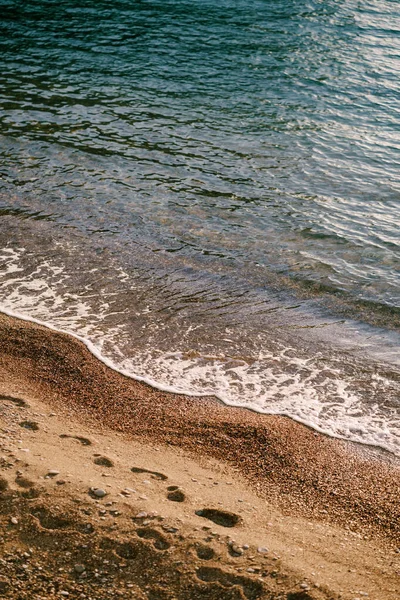 Fala toczy się po plaży, gdzie widoczne są ślady ludzkich stóp. — Zdjęcie stockowe